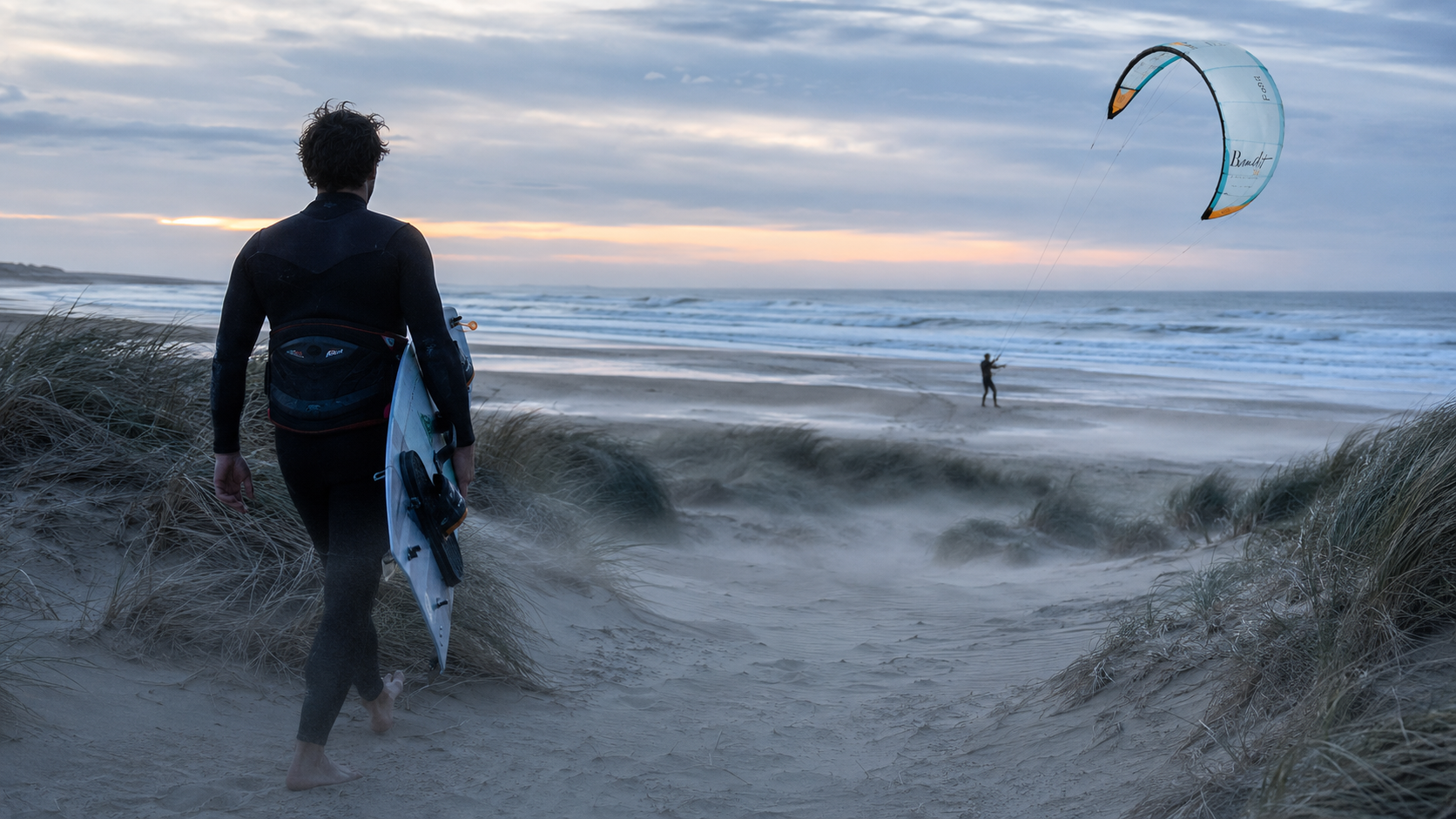 Rider walking the beach at sunset with board and kite in the air